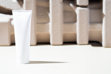 Abstract cosmetic white tube, cream or gel, against a backdrop of geometrically arranged cardboard pieces. The beauty and skincare industry.