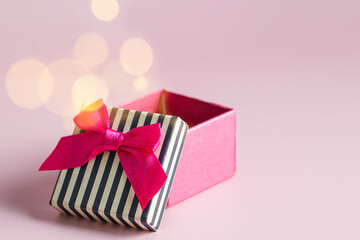 Open pink box with black stipes and red bow on pink background with bokeh, Gifting and surprise...