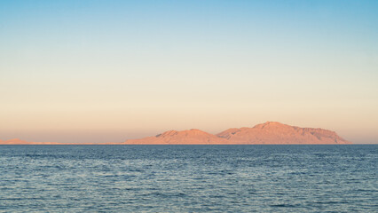 Serene seascape at dusk with gentle waves and a clear view of distant mountains under a soft sky.