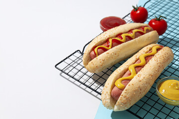 Hot dogs on grid, sauces in bowls and tomatoes on white and blue background, space for text