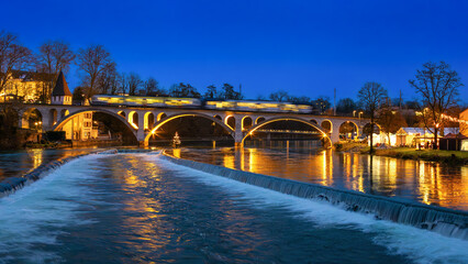 A train crosses the Reuss River Bridge to Bremgarten, Switzerland, during the blue hour in...