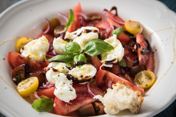 Italienischer Burrata Käse Salat mit bunten roten und gelben Tomaten, Basilikum, Olivenöl und Balsamico Dressing in tiefer Teller