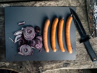 Cutting board on an outdoor wooden camping table with cut red onion, mushroom, garlic, black...