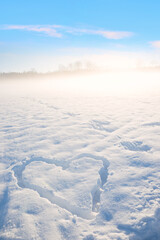 snow covered field with carved love heart, morning fog and blue sky above