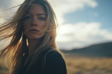 A woman with flowing hair stands in the vastness of a desert, her intense gaze and the wind's...
