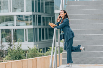 business woman talking on mobile phone on the street with documents