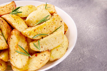 Baked potato wedges with seasonings on a plate on a gray stone.