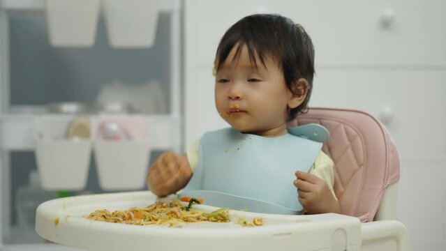 infant baby eating food and vegetable by self feeding BLW or baby led weaning on a chair