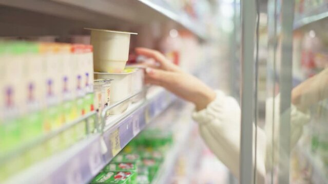 The hands of a girl-buyer take a container with a dairy product from the shelf