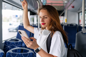 Female passenger stands inside the bus and using smart phone. - obrazy, fototapety, plakaty
