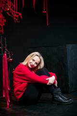 Obraz na płótnie Canvas A positive blonde woman in New Year's red clothes in an atmospheric photo studio with a stylish festive interior in red colors.