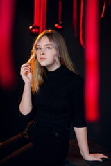 A beautiful young blonde girl in New Year's black clothes in an atmospheric photo studio with a stylish festive interior in red colors.