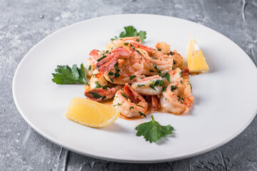 Fried Argentine shrimps with garlic and herbs on a white plate with lemon. 