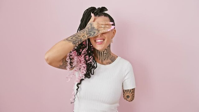 Cheerful hispanic amputee woman playfully covers eyes, standing isolated over pink background. surprise peek-a-boo with a confident smile.
