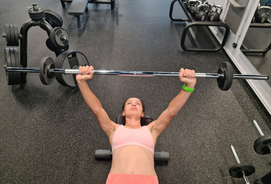 Woman pressing barbell while lying on bench in gym