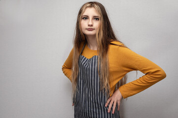 Portrait of young teenage girl in yellow shirt and classic black and white stripe apron on light...