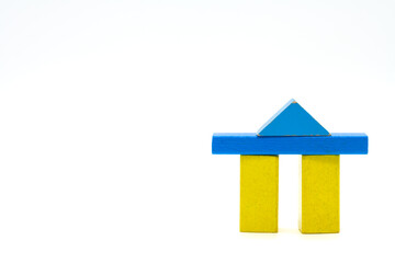 Two yellow wooden blocks with blue crossbar and triangle as a roof standing on a white background