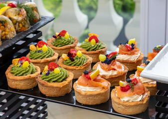 Delicious gourmet tartlets with avocado spread and smoked salmon adorned with colorful garnishes, elegantly presented on a modern catering display