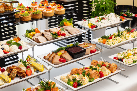 Elegant buffet spread featuring a variety of gourmet dishes including canapes, salads, meat platters, and desserts beautifully arranged on tiered trays