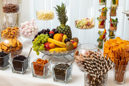 Assorted desserts and fresh fruit display at a party with marshmallows, cookies, and fruit skewers set on a white tablecloth