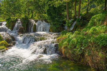 Fototapeta na wymiar A small waterfall in a stream which runs through the village of Martin Brod in Una-Sana Canton, Federation of Bosnia and Herzegovina. Located within the Una National Park. Early September