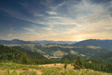 Panoramic view of rolling hills with forest under a blue sky at sunset.