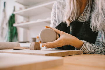 Female hands working with clay makes ceramic tableware on pottery workshop. - obrazy, fototapety, plakaty