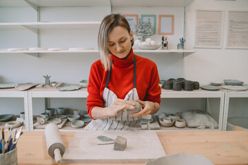 Female craftsperson working on ceramics tableware on pottery workshop.