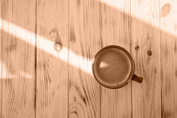 Background with color of the year -2024. Trendy color peach fuzz. Cup of coffee on a light wood...
