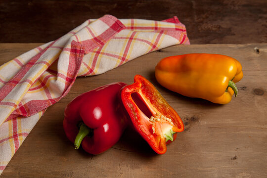 Whole and half red and yellow bell pepper on wooden background with red kitchen towel. .
