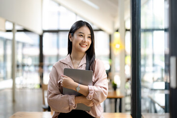 Smiling asian woman stands holding laptop computer in office.