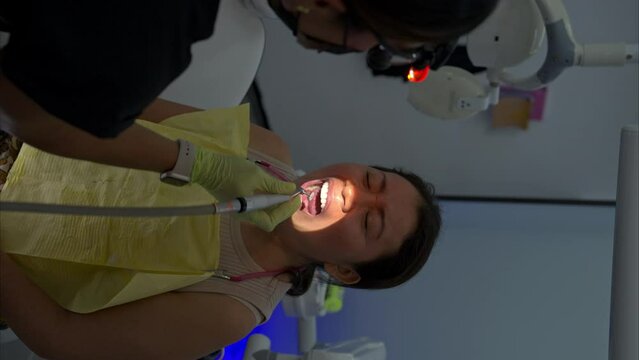 Vertical slow motion of a dentist filing a patient's new set of veneers with a dental bur