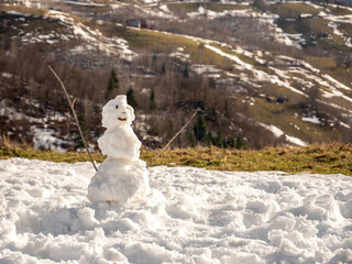 small snowman sitting in a meadow with springtime like surroundings 