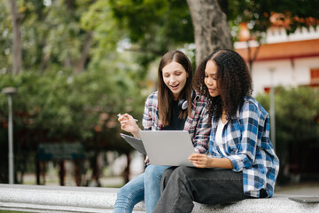 Young college students focusing on his school project, looking at laptop and tablet, discussing and working together at the campus park