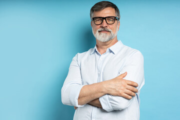 Bearded middle-aged man wearing glasses posing over blue studio background