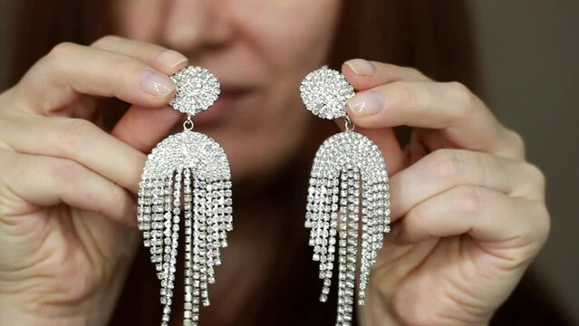 Closeup of a woman with wearing large jewelry earrings. Girl wearing luxury expensive jewelry with shining diamonds and precious stones. Female hands hold and showing earring.