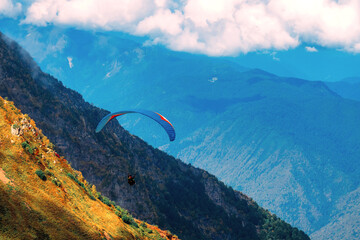 Paraglider flies in mountains. Beautiful view of mountain range with clouds. Extreme sport in...