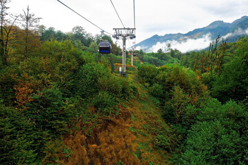 Cable car with cabin in mountains. Funicular. Sightseeing route or excursion for tourists in mountains on cloudy summer day.