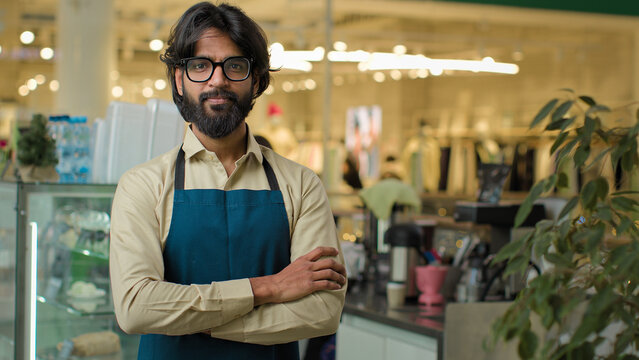 Happy smiling friendly cafe worker guy Indian male waiter in apron cafeteria working showing thumb up gesture like hand sign to client Arabian barista man at workplace catering service small business