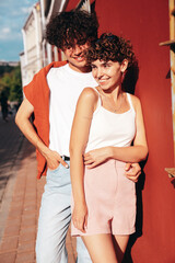 Young smiling beautiful woman and her handsome boyfriend in casual summer clothes. Happy cheerful family. Female having fun. Couple posing in street at sunny day. Near wall at sunset