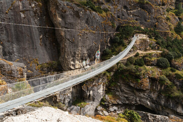 Fototapeta premium Landscape with Suspension Bridge over Bhote Kosi River during Three passes trekking in Sagarmatha national park, Nepal. A bridge with Guru Rinpoche images on rocks on the way to Thame.