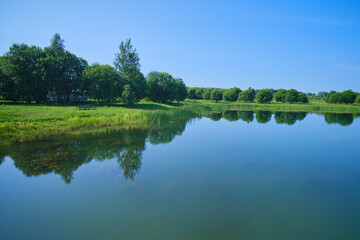 The blue water of a clear lake with a reflection of the sky and green trees