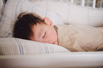 The two-year-old toddler baby is sleeping in his crib. Child boy is sleeping on a pillow in bed....