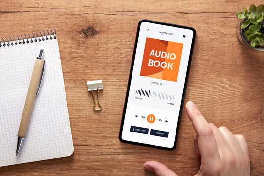 Overhead shot of hand with smartphone playing an audiobook over cozy workspace. Audio book app concept.