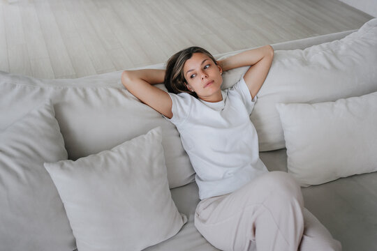 Frustrated young woman n casual sitting on couch in disappointed mood, feels apathy. Lonely American girl exhausted, emptiness.