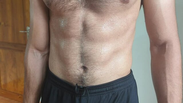 closeup pan video of a young athletic man flexing his abs and muscles after an intense workout training in the gym
