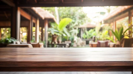 Tuinposter An empty wooden table foregrounds a blurred Balinese-style interior, inviting a serene and tropical atmosphere perfect for a calm setting. © Alina Nikitaeva