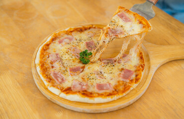 Cheese Pizza with delicious yellow bacon on the wooden dining table where the pizza scoop was about to be scooped and eaten