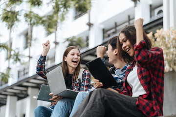Happy group of college students use laptop feel excited overjoyed triumph with good news over smartphone or Tablet.