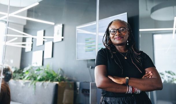 African business woman stands outside a conference room with crossed arms